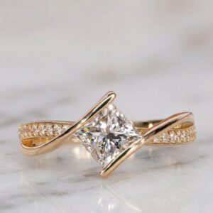 Unique modern engagement ring featuring a dazzling princess cut diamond centerpiece set on a graceful twisted crossover design, accented with sparkling pavé stones along a sleek 14K yellow gold band, offering a bold contemporary style with elegant curves, radiant brilliance, and eye catching sophistication