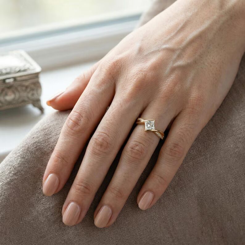 Unique modern engagement ring featuring a dazzling princess cut diamond centerpiece set on a graceful twisted crossover design, accented with sparkling pavé stones along a sleek 14K yellow gold band, offering a bold contemporary style with elegant curves, radiant brilliance, and eye catching sophistication - Image 2