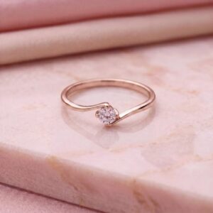 Minimalist curved solitaire engagement ring with a petite round-cut diamond, set in 14K rose gold, featuring a delicate wave design, modern feminine style, and soft elegant sparkle